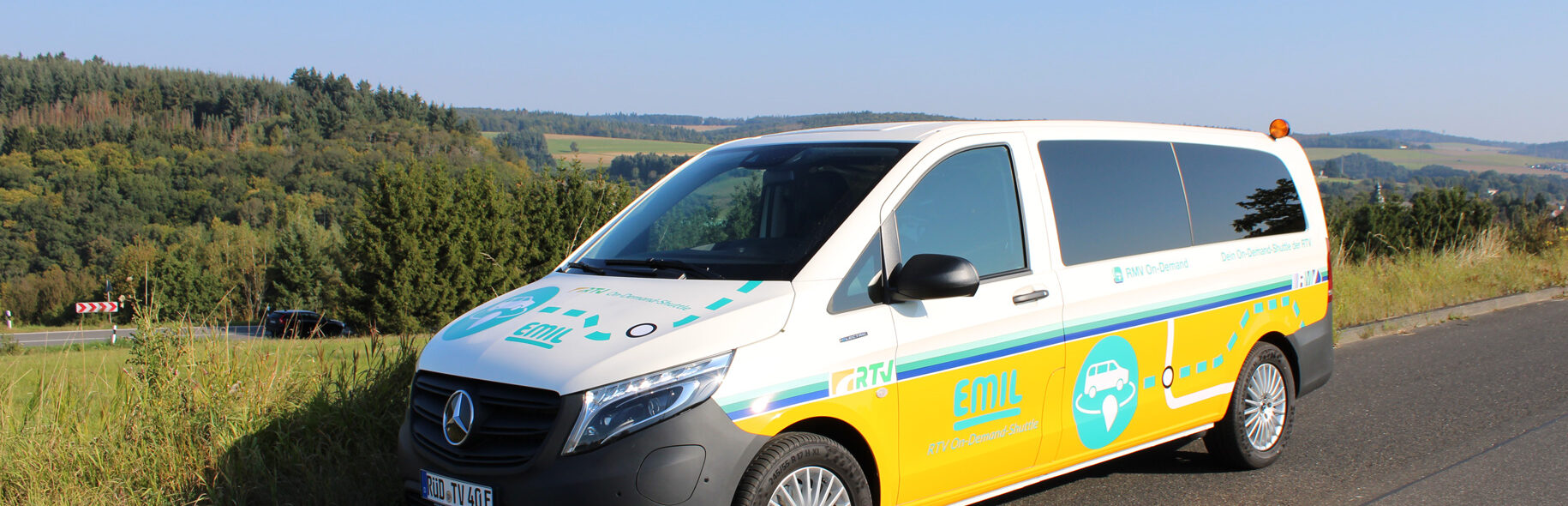 Das elektrisch betriebene On-Demand-Shuttle „EMIL“ der Rheingau-Taunus-Verkehrsgesellschaft steht vor dem historischen Idsteiner Schloss mit weiß-roter Fassade und markantem Schieferdach.